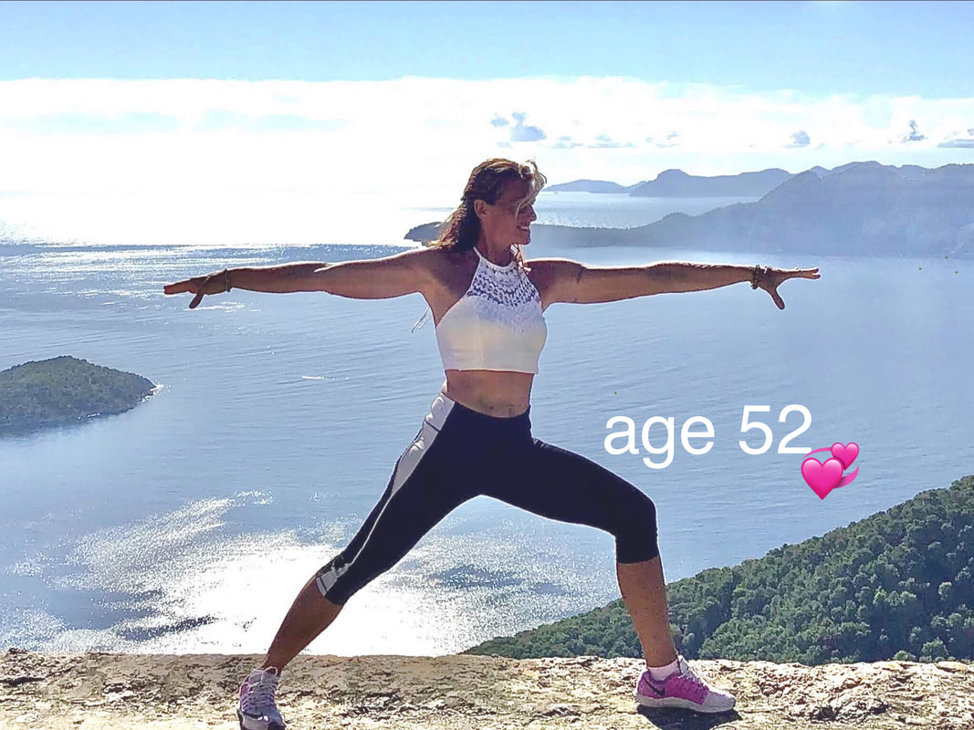 Sandra Van Olmen holding a steady warrior pose on a clifftop high above the Mallorca bay, islands and headland behind her